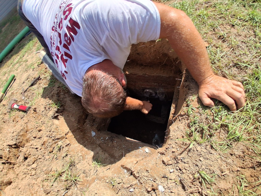 Crew member reaching down into an open septic access hole