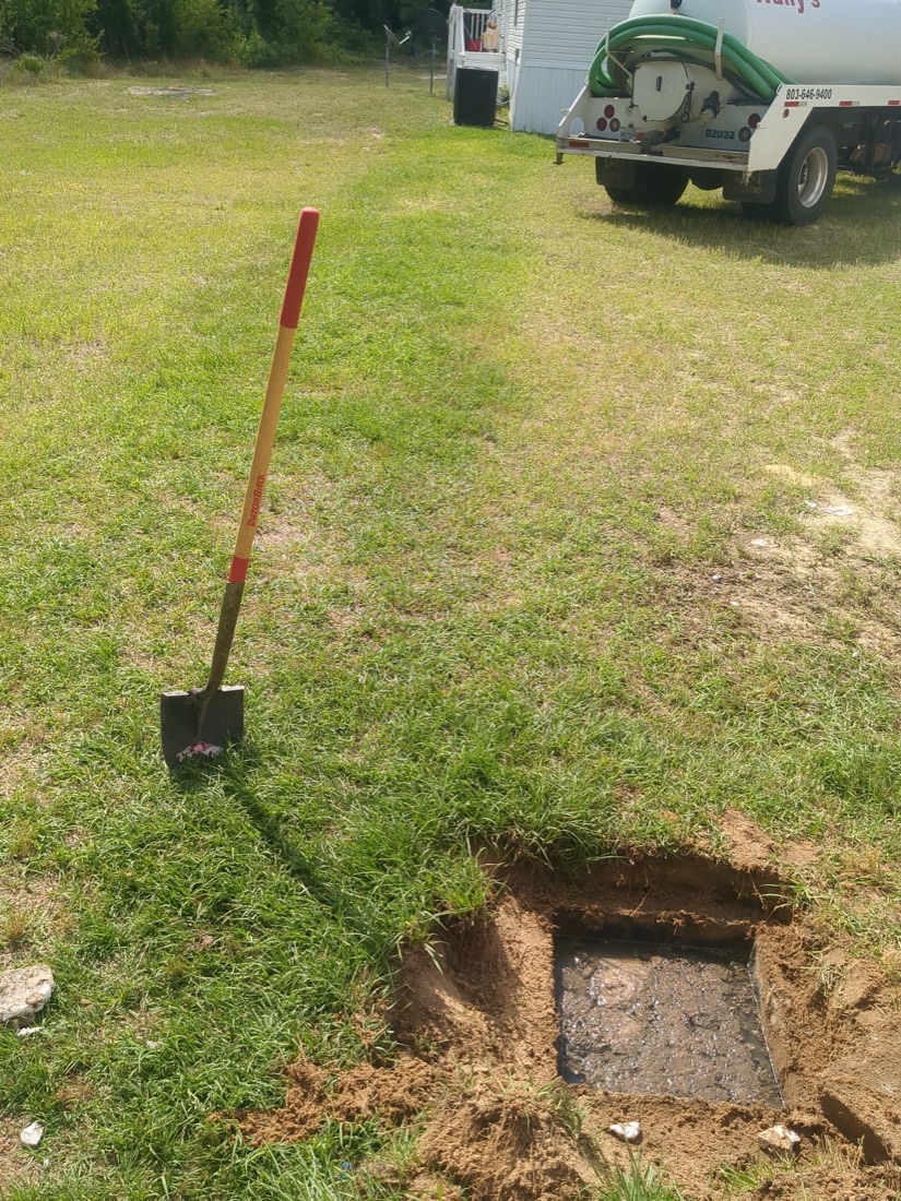 Shovel standing beside a freshly uncovered septic riser lid in a Wagener area lawn